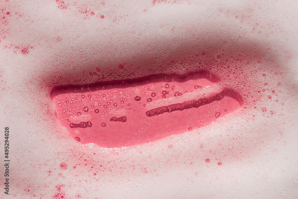 Fototapeta premium Foam on a pink background. Soapy liquid texture with bubbles. Natural sunshine and shadows. Skincare cleansing cosmetic in top view.