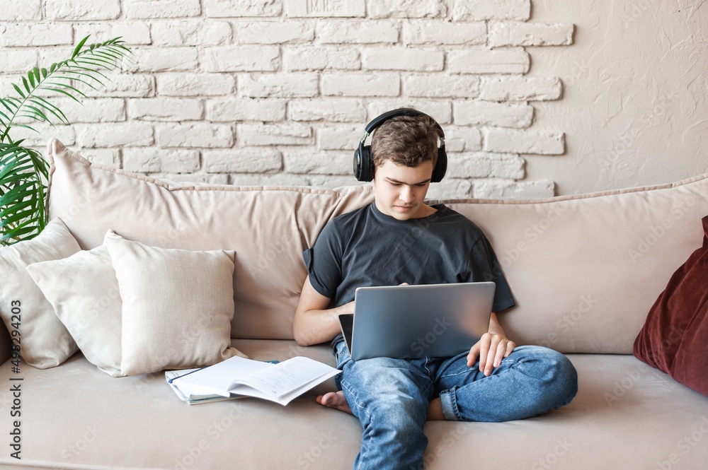 A teenage boy in headphones and with a laptop to learn and communicate via video conference with peers and teachers. Home and distance learning. Courses for schoolchildren.