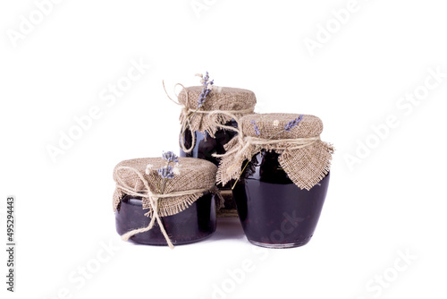 Sweet homemade blackberry jam in small beautiful glass jars decorated with Lawanda flower branches on white isolated background.