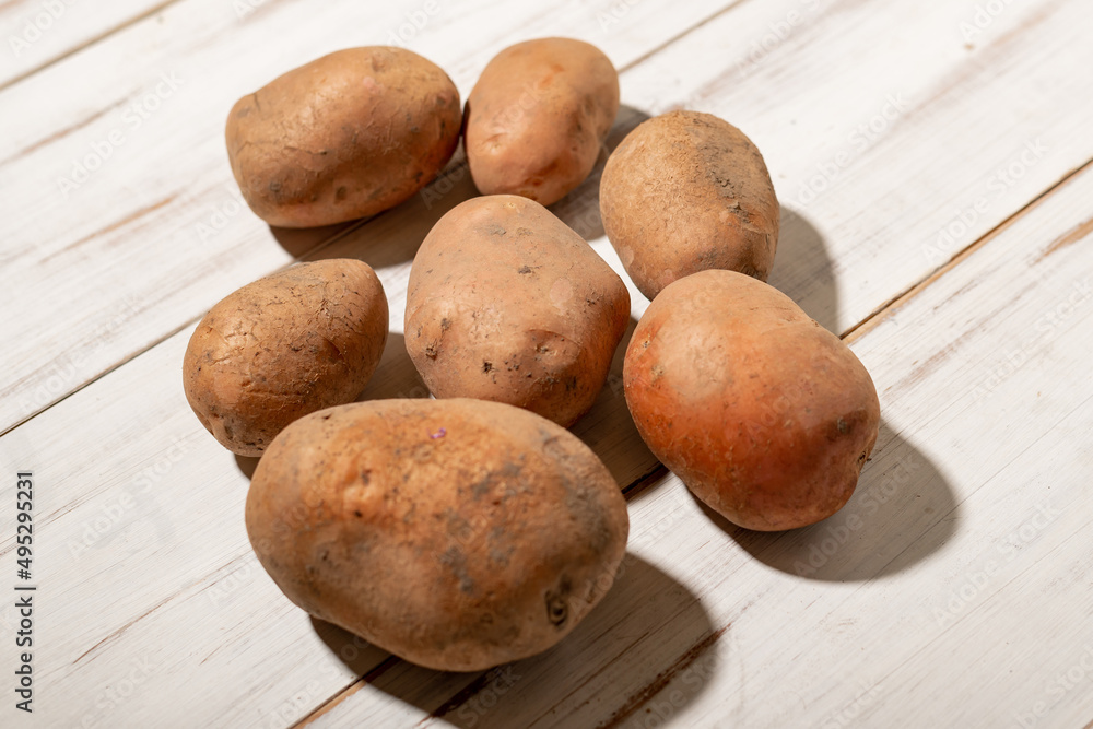 Raw potato tubers on a light wooden background. Unpeeled dirty potatoes. Raw potato tubers on a light wooden background. Unpeeled dirty potatoes.
