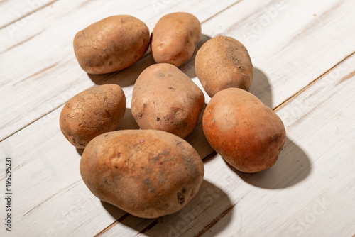 Raw potato tubers on a light wooden background. Unpeeled dirty potatoes.