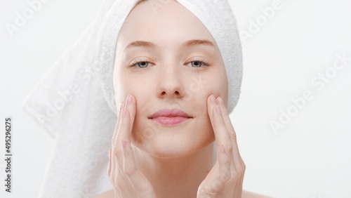 Big close-up shot of young ginger Caucasian woman with a towel on her head touches her cheeks with both hands on white background | Skin elasticity commercial concept
