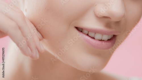 Extreme close-up of beuty woman's face with smooth healthy skin, hand touching jawline on pink background | Skincare and face care commercial concept 