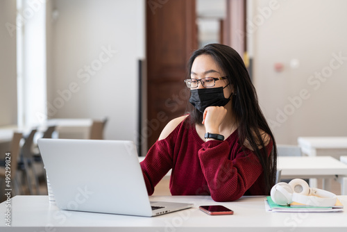 Young girl wear medical mask sit at university class study on laptop. Female asian student in protective facemask inside college classroom in covid-19 pandemic. Education and new normality lifestyle