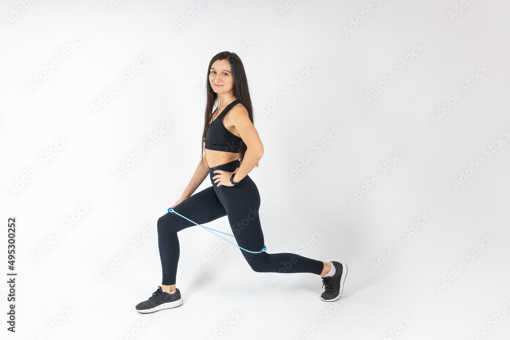 Sportswoman exercising with resistance band on white background. Attractive brunette woman in fashionable sportswear exercising. Healthy lifestyle, sport concept, Full length view Sportswoman exercising with resistance band on white background. Attractive brunette woman in fashionable sportswear exercising. Healthy lifestyle, sport concept, Full length view