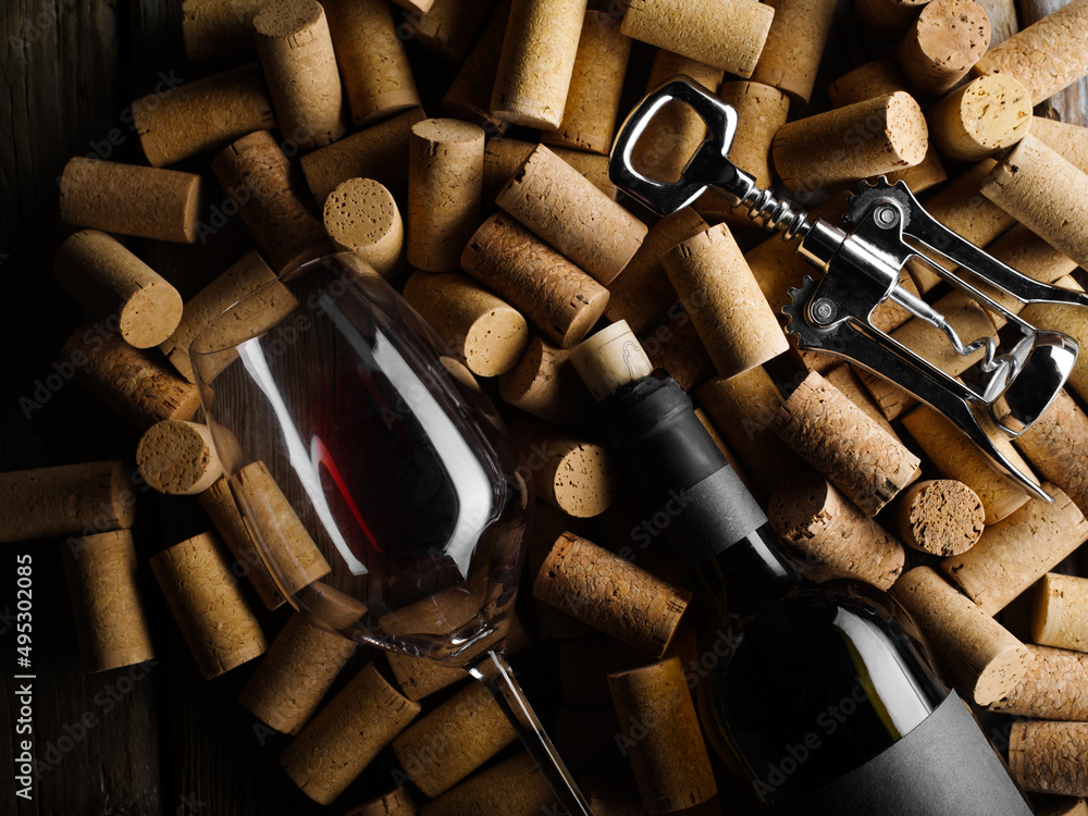 Festive composition. On wine corks lies a bottle of red wine, a corkscrew and a wine glass. There are no people in the photo. Low angle view. Wine collection, tasting, wine cellar.