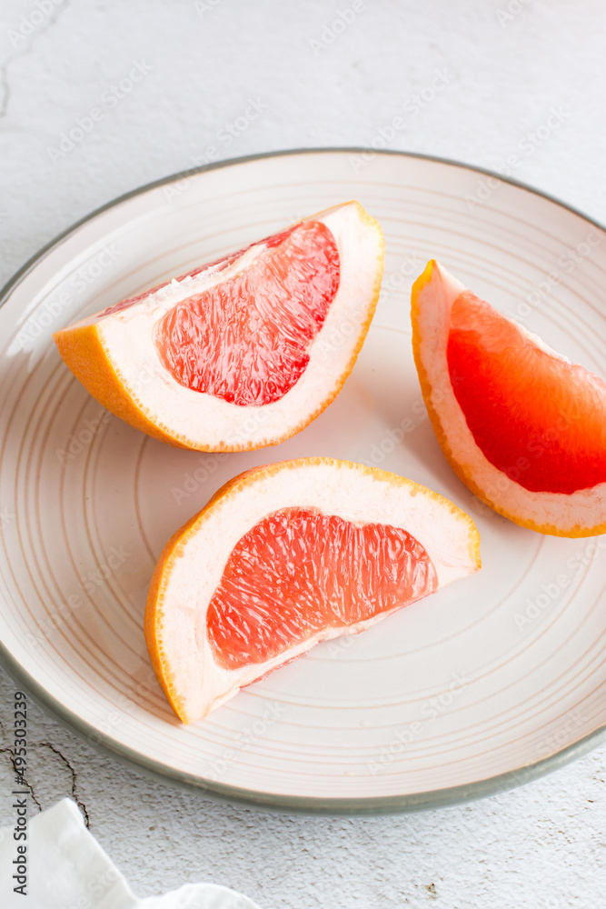 Ripe grapefruit slices on a plate on a light table. Sustainable food  lifestyle. Vertical view. Close-up
