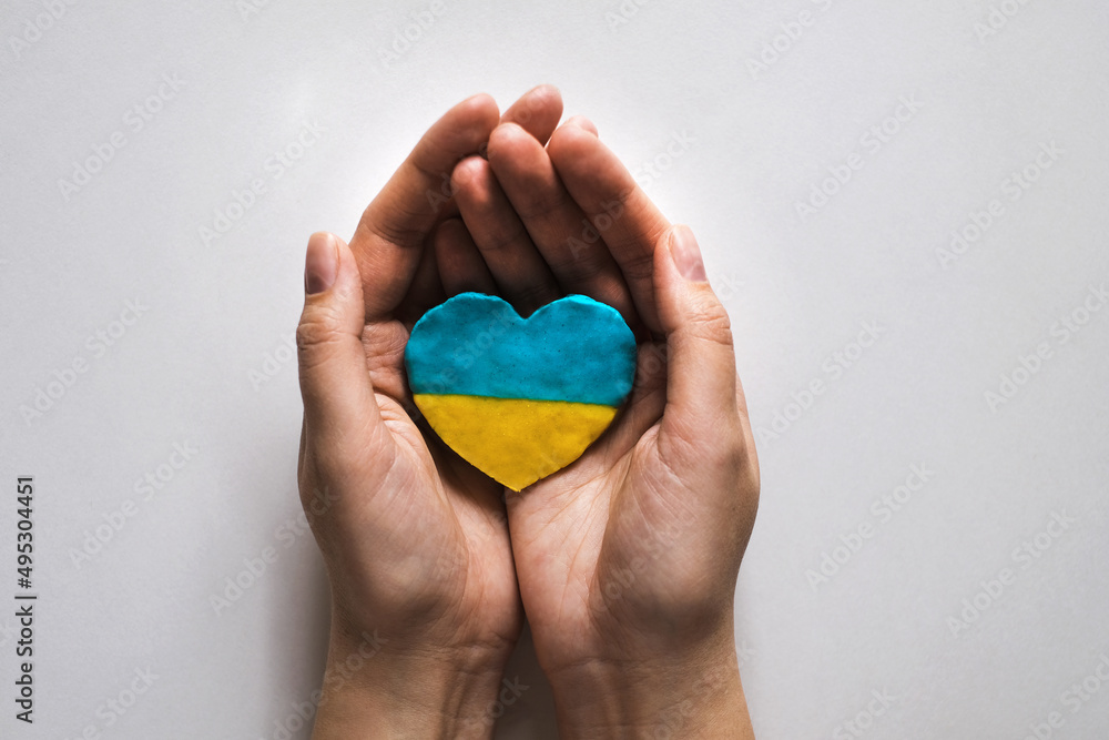 a woman in her palms holds a heart in the color of the flag of Ukraine. Support for Ukraine in the war with Russia a woman in her palms holds a heart in the color of the flag of Ukraine. Support for Ukraine in the war with Russia