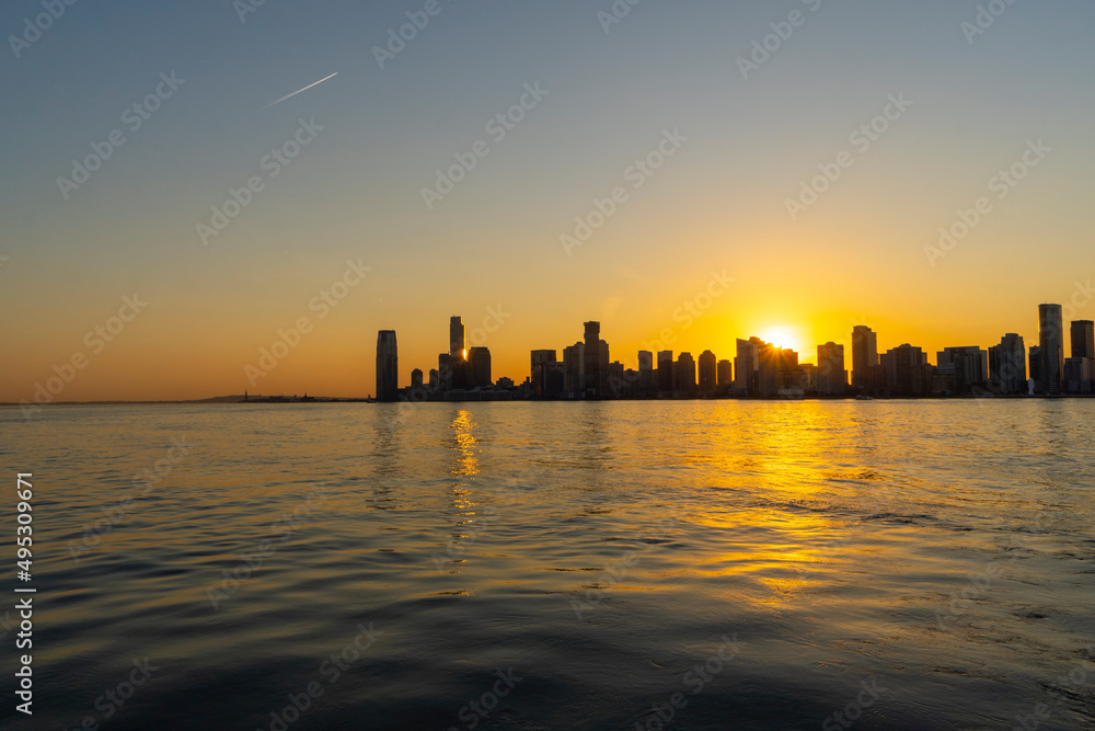 The sun sets in New Jersey skyscraper beyond Hudson River from Hudson River Park in Manhattan ward on November 09, 2021 in Jersey City New Jersey USA.