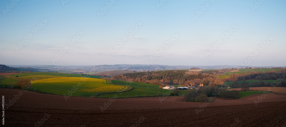 panoramic view of rolling english countryside with blue sky and green fields and brown muddy ploughed fields