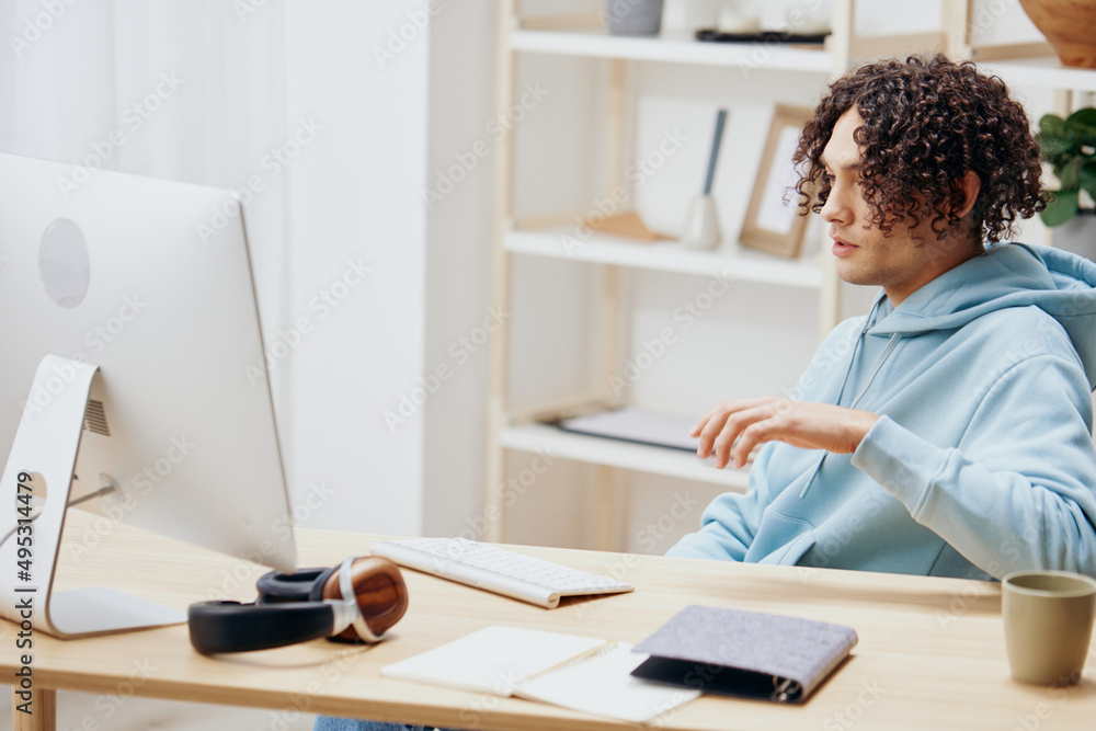 A young man sitting at a table in front of a computer freelance interior A young man sitting at a table in front of a computer freelance interior
