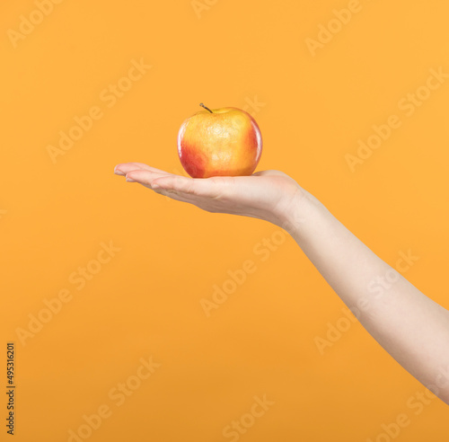 a pink-yellow apple lies on an open female palm on a yellow background close-up