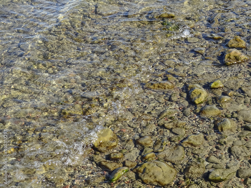 Selective focus of pebble, brown small stones under transparent seawater of Baltic sea on a sunny day