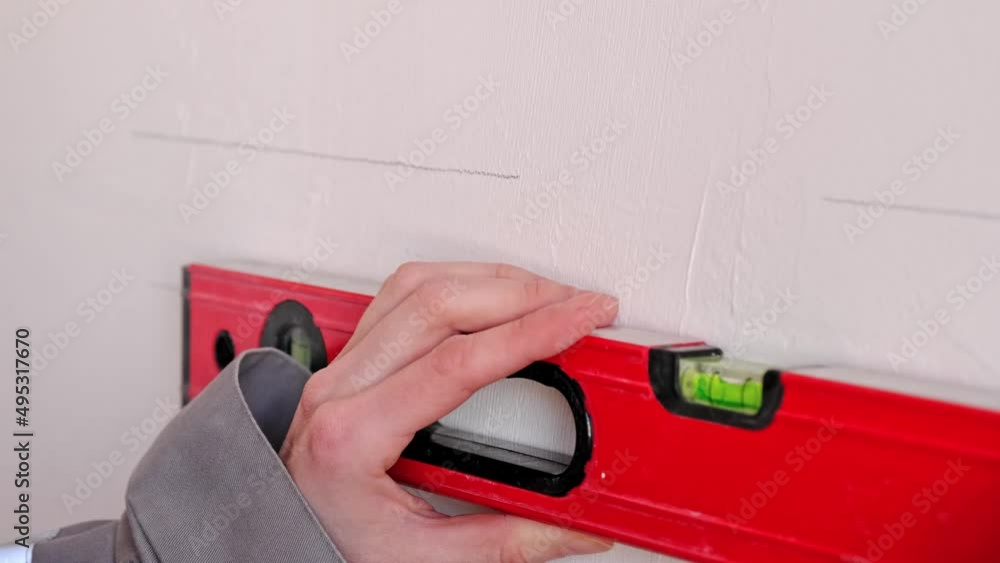 Drawing horizontal markings on the wall by level - DIY home repair. A woman in a red baseball cap and construction uniform is preparing the finishing of the walls Drawing horizontal markings on the wall by level - DIY home repair. A woman in a red baseball cap and construction uniform is preparing the finishing of the walls