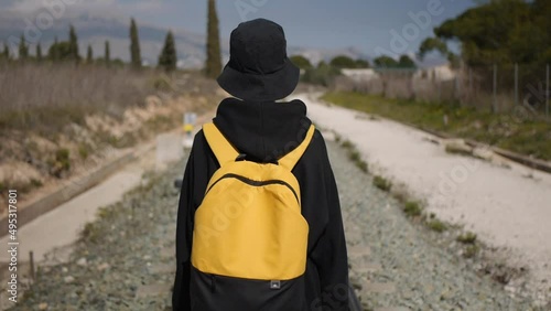 a teenage girl in black hat with yellow backpack walking along the railroad tracks. Tracking shot