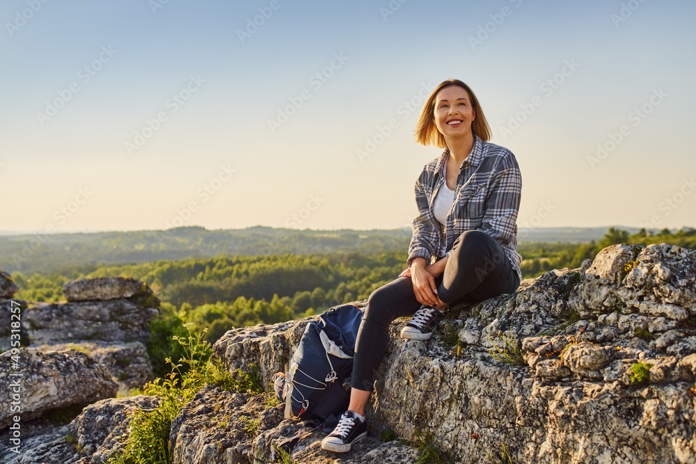 Happy woman hiker sitting on rock at top of the mountain enjoying summer hike Happy woman hiker sitting on rock at top of the mountain enjoying summer hike