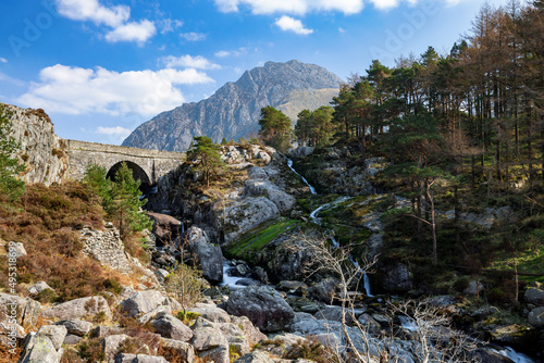 Mount Tryfan in Ogwen Valley sits in the background as a waterfall runs alongside an arched stone bridge