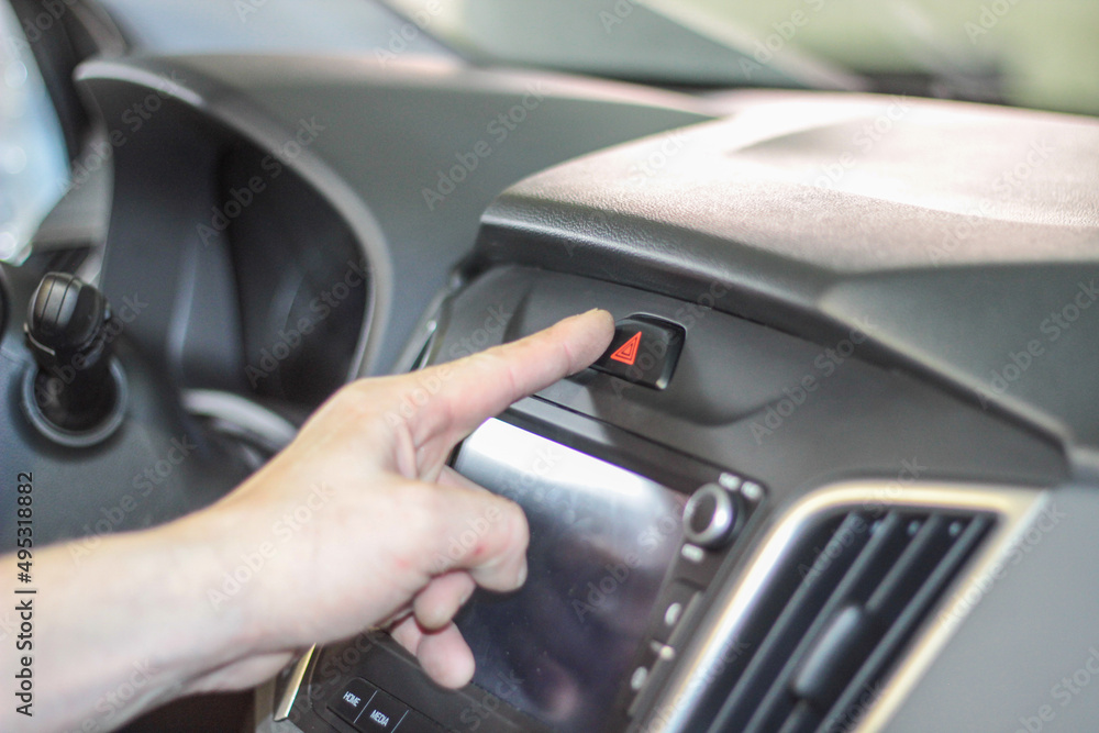 Closeup of man's hand pressing emergency stop button in car. using human hand to push the hazard lights button on the font console controller of the vehicle for emergency situation while driving a car