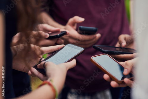Lets see what our other friends are doing. Closeup of a group of young unrecognizable people standing in a circle while browsing on their mobile phones outside during the day.