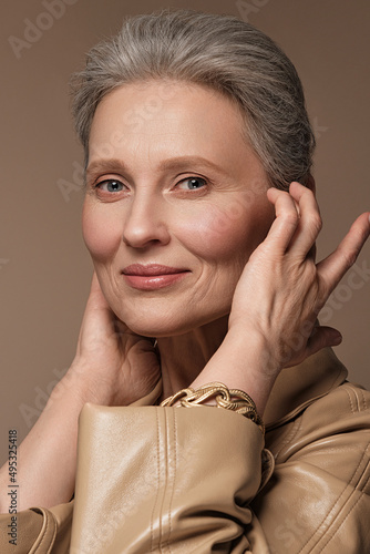 Portrait of a beautiful elderly woman in a beige raincoat with classic makeup and gray hair.