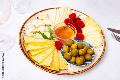 Various types of cheese, honey, raspberries and olives on a wooden board