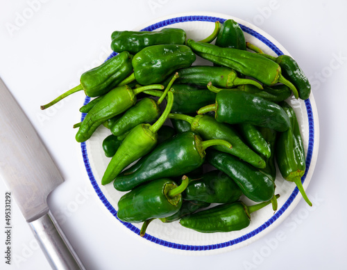 Plate full of fresh green padron peppers and steel kitchen knife on white background. Organic cooking ingredients.. photo