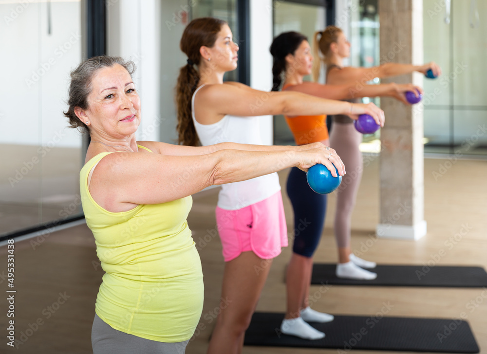 Portrait of mature female performing set of exercises with pilates balls during group class in fitness studio