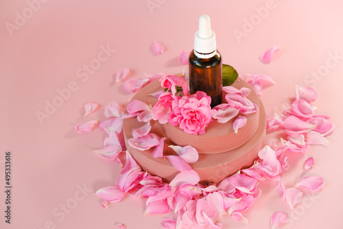 Rose essential oil in a glass bottle and rose flowers on a pink podium on a pink background.natural rose oil. Aromatherapy and cosmetics .