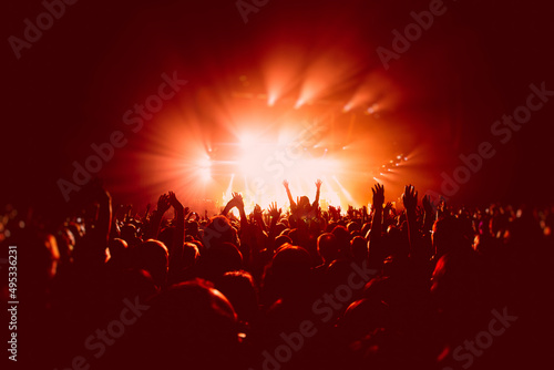A crowded concert hall with scene stage in red lights, rock show performance, with people silhouette, colourful confetti explosion fired on dance floor air during a concert festival © tsuguliev