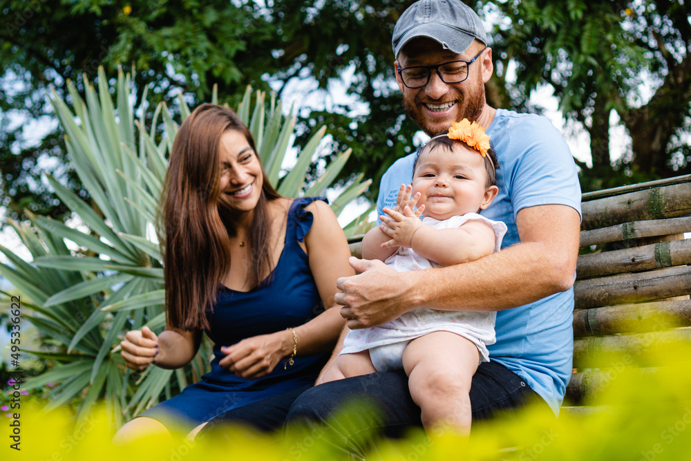 latin family smiling with a newborn baby girl on their lap, sitting in a park. latin family smiling with a newborn baby girl on their lap, sitting in a park.