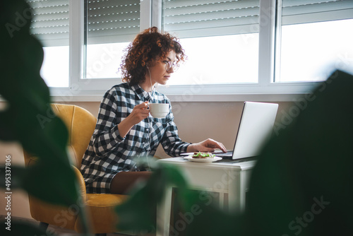 Side view of a curly business woman sitting indoos using laptop computer listening music with earphones. Morning coffee. Curly hair. Modern lifestyle. Side view photo