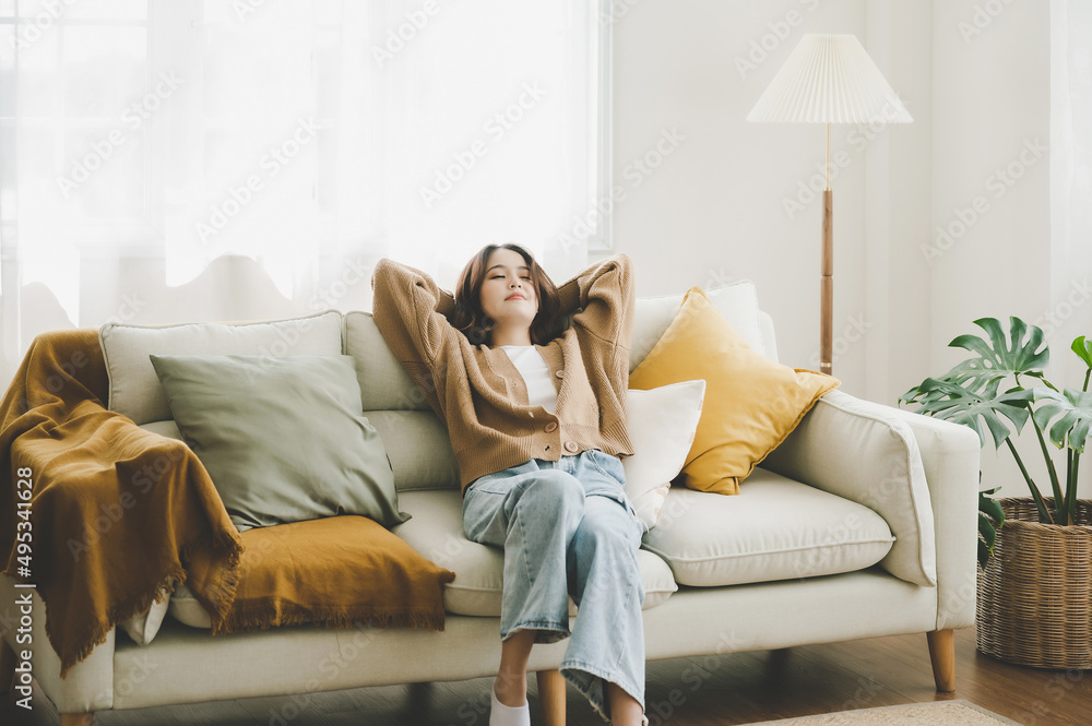 Happy asian woman relaxing on comfortable soft sofa enjoying stress free weekend at home, She stretching on couch thinking of pleasant lazy day
