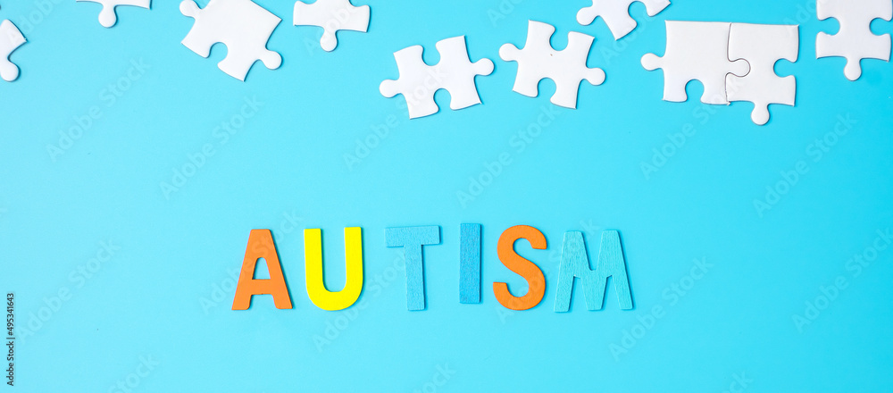 AUTISM text with white puzzle jigsaw pieces on blue background. Concepts of health, Autistic Spectrum disorder and world Autism awareness day AUTISM text with white puzzle jigsaw pieces on blue background. Concepts of health, Autistic Spectrum disorder and world Autism awareness day