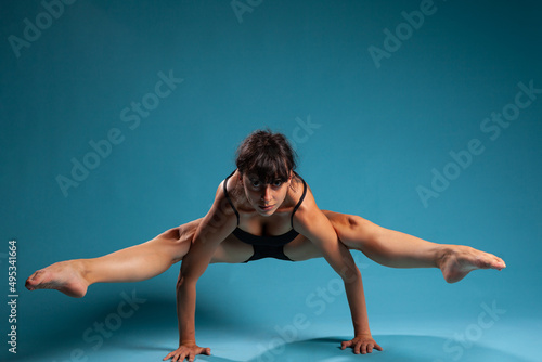 Personal trainer standing in hands stretching legs muscles practicing fitness position working at healthy lifestyle in studio with blue background. Active woman doing pilates workout