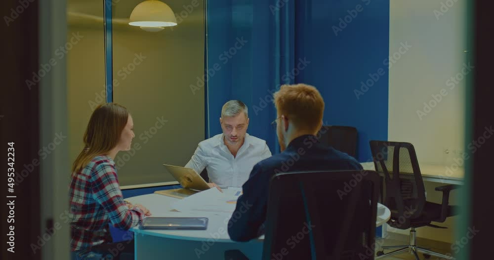 Young businessmen are sitting at a meeting in a modern coworking office and talking about the company's development plans. Gray-haired male business partner talks about sales growth indicators on Young businessmen are sitting at a meeting in a modern coworking office and talking about the company's development plans. Gray-haired male business partner talks about sales growth indicators on