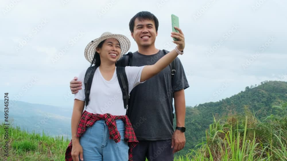 Man and woman travelers backpackers use mobile phones to take selfies on the mountain background. Hiking couple relaxing in nature on vacation. Man and woman travelers backpackers use mobile phones to take selfies on the mountain background. Hiking couple relaxing in nature on vacation.