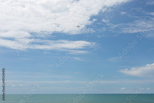 Passenger plane flying over blue ocean. Blue sky with white cloud background