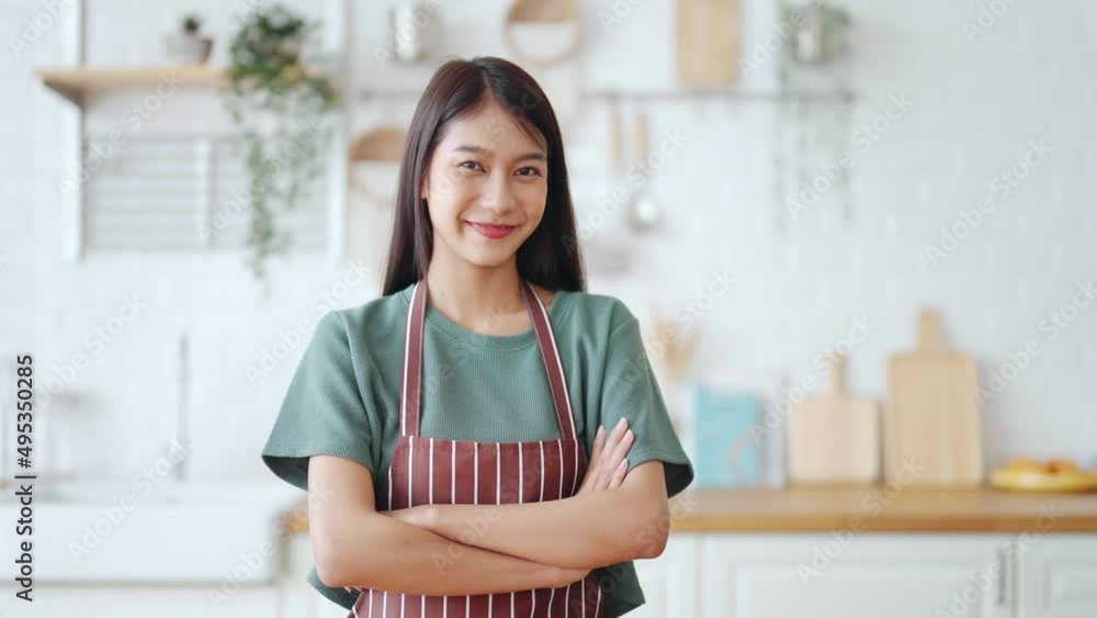 Happy young asian woman wearing apron and standing in kitchen room. Beautiful female smiling and looking at camera feeling confident Happy young asian woman wearing apron and standing in kitchen room. Beautiful female smiling and looking at camera feeling confident