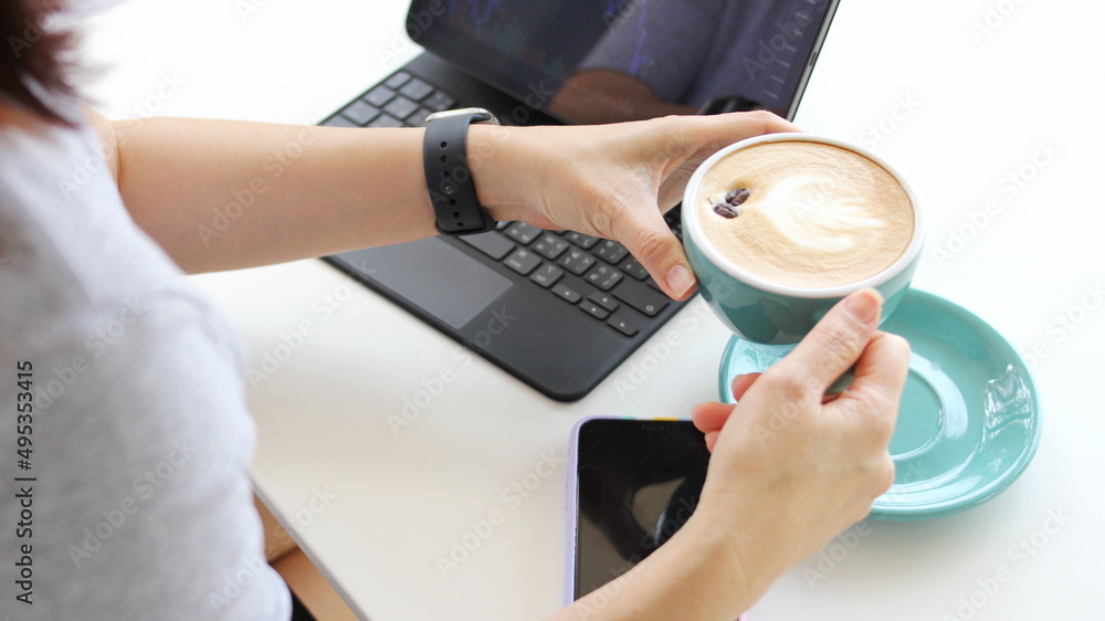 Woman's hand with a cup of coffee, sitting in the morning doing work with a laptop