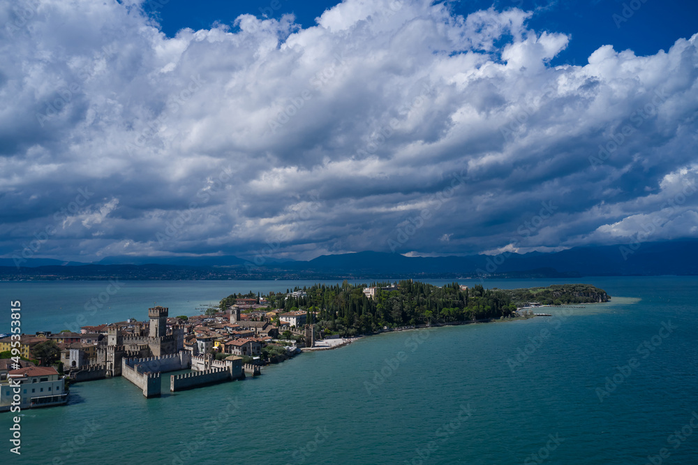 Rocca Scaligera Castle in Sirmione. Aerial view on Sirmione sul Garda. Italy, Lombardy. Cumulus clouds over the island of Sirmione. Panoramic view at high altitude. Aerial photography with drone.