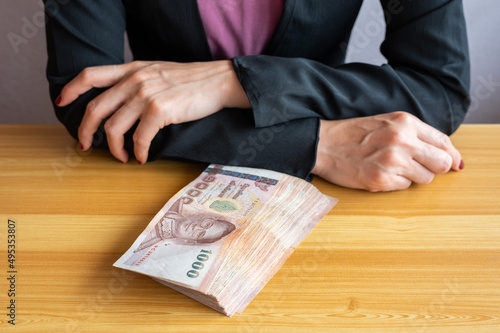 An accountant woman sitting and cross her arms before counting or giving Thai baht banknotes to someone. The baht is the official currency of Thailand.