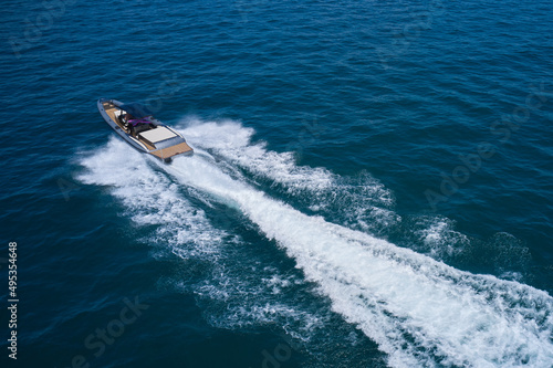 Boat drone view. Speedboat moving fast on blue water aerial view. Dark gray blue boat in motion at sea.