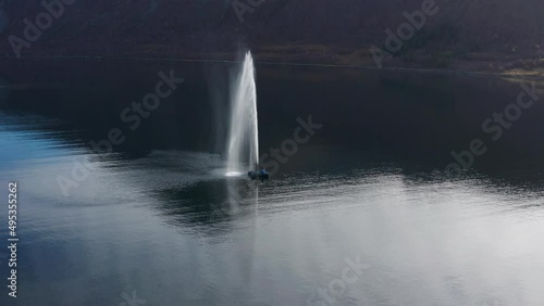 A fountain in the fjord near the small fishing village of Torsken, Norway. The sky is reflected in the mirrorlike still waters. Mountains tower in the background. Slow-motion, orbit, aerial. photo