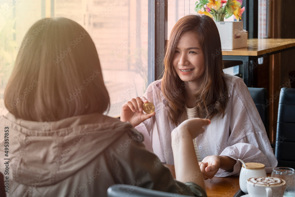 Beautiful Asian woman in work clothes smiling and holding bitcoins. Talk to customers in a cafe. Online business concept.