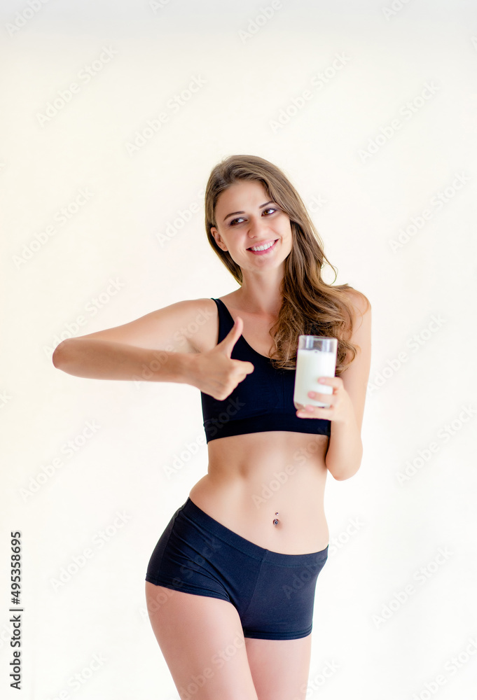 Smiling young woman beautiful slim figure holding a glass of milk, wearing a black dress, exercising
