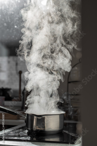 Boiling water with steam in a pot on an electric stove in the kitchen. Blurred background, selective focus.