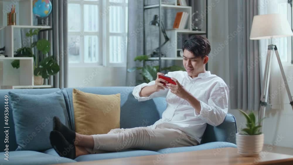 Full Body Of Asian Man Playing Game On Smartphone And Smiling While Lying On Sofa In The Living Room
Full Body Of Asian Man Playing Game On Smartphone And Smiling While Lying On Sofa In The Living Room