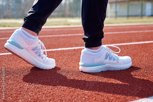 Male runner feet with white sneakers at stadium track, close up. Sport sneakers for jogging. Fitness and healthy lifestyle concept