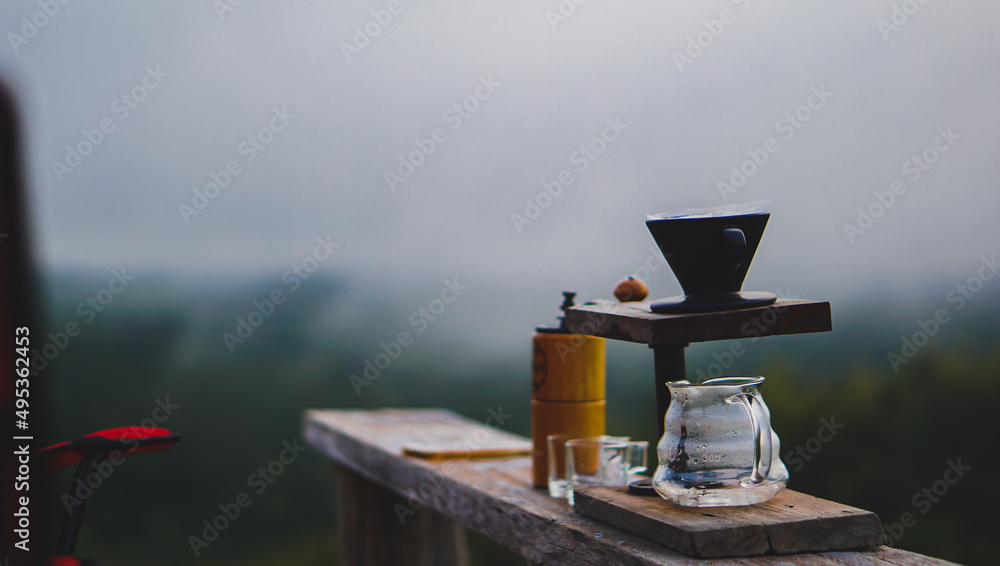 Naklejka premium Drip coffee set on wooden table with mountain landscape on dark tone