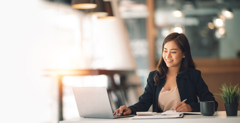 Young asian beautiful and charming busineswoman smiling and working on laptop computer at office.